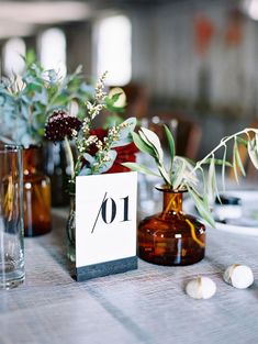 the table numbers are displayed in vases with flowers and greenery on them, along with candles