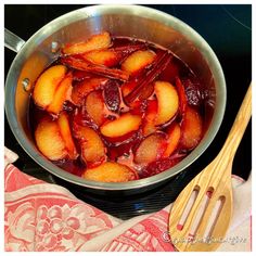 a pan filled with fruit sitting on top of a stove next to a wooden spoon