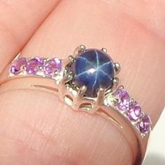 This delicate ring is a size 6 1/2, Sterling Silver, Blue Star Sapphire, with 6 bright purple, faceted Amethysts on the band, 3 on each side of the center stone. This charming little ring would make a treasured gift, a promise ring, or even an engagement ring. Star Sapphire Ring Purple, Blue Star Sapphire Ring, A Promise Ring, Star Sapphire Ring, Blue Star Sapphire, Star Sapphire, Silver Work, Bright Purple, Delicate Rings