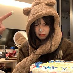 a woman in a bear costume holding a cake with frosting on it and pointing at the camera