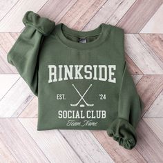 a green sweatshirt that says rinkside social club with crossed sticks on the front