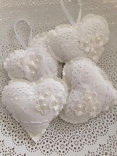 three white heart shaped ornaments with pearls and bows on a lace doily tablecloth