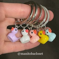 a person is holding five different colored key chains in their hand, one has a rubber duck and the other has a plastic chicken