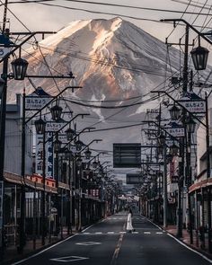 an empty street in front of a mountain with power lines running across it and buildings on both sides