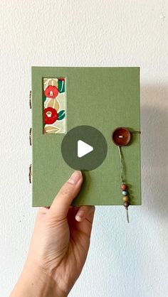 a person holding up a green book with buttons and string attached to the front cover