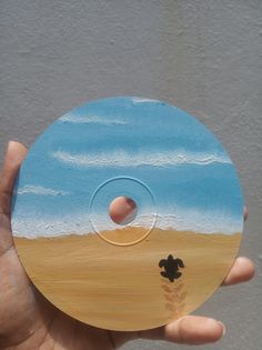 a person holding up a wooden disc with a painting on it