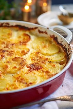 a red casserole dish filled with potatoes on a table next to silverware