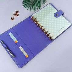 a blue notebook and pen sitting on top of a white table next to a plant