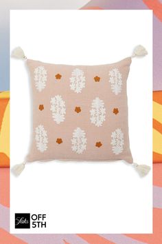 a pink pillow with white flowers and tassels on the front, sitting against a colorful background