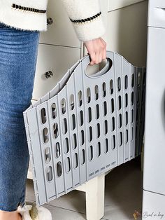 a woman is holding a gray basket in front of a washer and dryer