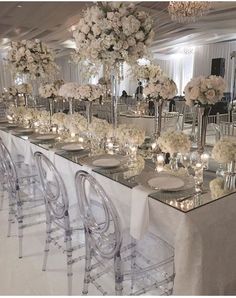 the wedding reception table is set up with clear chairs and white flowers in vases