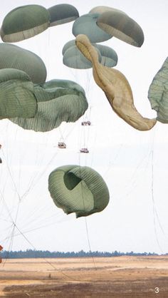 several large green kites being flown in the air over an open field with vehicles