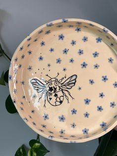 a blue and white flowered bowl with a bee painted on the side, sitting next to a potted plant