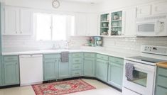 a kitchen with green cabinets and white appliances, including an oven, dishwasher, microwave, sink, and rug