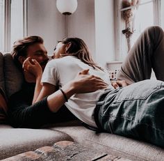 a man and woman laying on top of a couch next to each other in front of a window