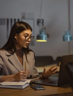 a woman sitting at a desk in front of a laptop computer holding a pencil and paper