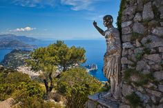 a statue on top of a stone wall next to trees and the ocean in the background