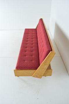 a red bench sitting on top of a white floor next to a wooden frame and wall