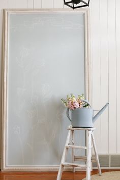 a flower pot sitting on top of a wooden stool next to a white framed wall