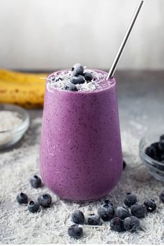 a blueberry smoothie in a glass with a straw and some blueberries around it