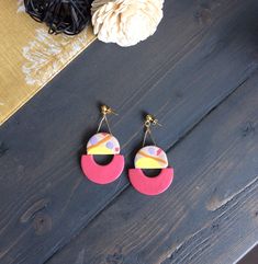 two pairs of pink, yellow and red earrings on top of a wooden table next to a flower