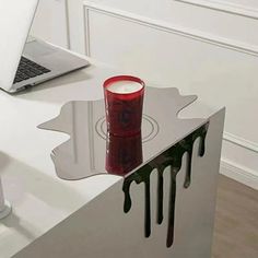 a laptop computer sitting on top of a desk next to a red cup with liquid pouring out of it