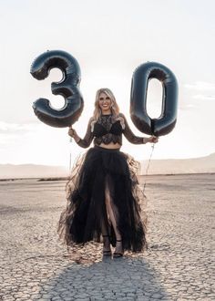 a woman in a black dress is holding two large balloons and posing for the camera