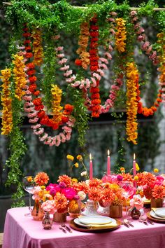 a table topped with lots of flowers and plates filled with food next to hanging candles