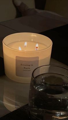 a lit candle sitting on top of a table next to a glass filled with water