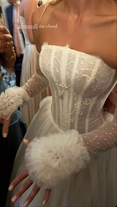 a woman in a white wedding dress with feathers on her arm and gloves around her waist