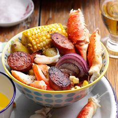 a bowl filled with meat, vegetables and corn on the cob next to a glass of orange juice