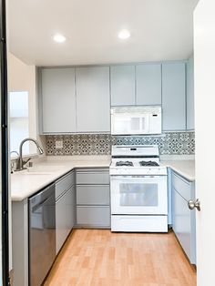 an empty kitchen with white appliances and wood flooring in front of the stove top oven