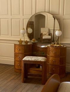 an antique dressing table with mirror and stool in a room that has white paneling on the walls