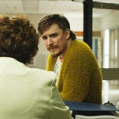 a man sitting at a table talking to a woman who is wearing a yellow sweater