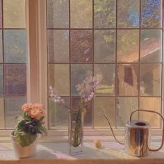 two vases filled with flowers sitting on top of a window sill next to a watering can