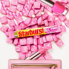 a pink purse with some candy on top of it next to other items that include lipstick and nail polish