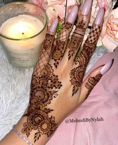 a woman's hand with henna on it next to a candle and flowers