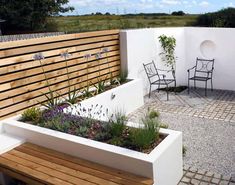 a wooden bench sitting in the middle of a garden next to a white wall and fence