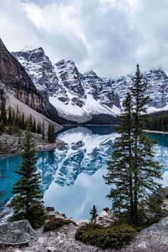 a lake surrounded by snow covered mountains and pine trees in the foreground with blue water