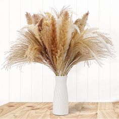 a white vase filled with dry grass on top of a wooden table