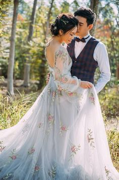 a man and woman standing next to each other in front of trees wearing wedding dresses