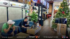 two people sitting on couches in a room with christmas trees and televisions behind them