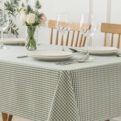 the table is set with plates, glasses and flowers in vases on top of it