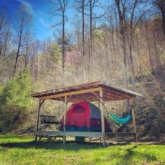 a tent in the woods with a hammock hanging from it's roof