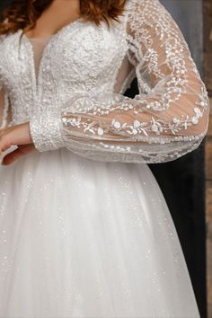 a woman wearing a white wedding dress with long sleeves and beading on her arms