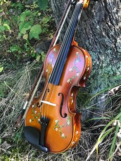 an old violin that is sitting in the grass next to a tree with flowers painted on it