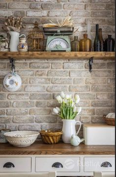 a brick wall with white flowers and dishes on it, along with other kitchen items