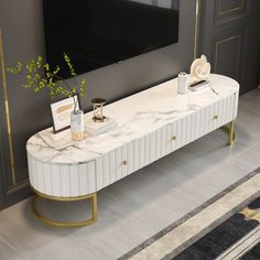 a white marble console table with gold legs and two vases on it in front of a flat screen tv