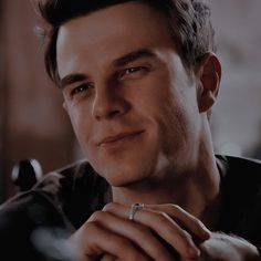 a man with a ring on his finger looking at the camera and smiling while wearing a black shirt