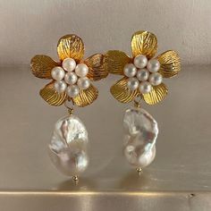 Make a bold statement with our exquisite huge gold floral stud earrings featuring dazzling baroque pearls. Choose between the two large gold floral studs adorned with faux tiny pearls one measuring approximately 28mm and the other  36mm. The suspended dangling baroque pearls are medium to large -sized ranging from 13mm to 15mm (w) to 21mm to 23mm (l). Each white, lustrous pearl is carefully wire wrapped to perfection. These earrings are true showstoppers, perfect for weddings where you want to captivate attention or photo shoots where you want to stand out. Select your preferred design and elevate your style effortlessly. Price remains the same for both options. Note: you will receive actual pair of baroque pearls as shown on images.  These are huge gold floral studs Material:  Genuine cul Gold Flower Earrings With Pearl Drop For Party, Gold Pearl Drop Flower Earrings For Party, Chic Gold Flower Earrings For Wedding, Gold Pearl Earrings With Flower Shape For Party, Chic Handmade Gold Pearl Earrings, Gold Bridal Earrings With Pearl Drop In Flower Shape, Gold Bridal Earrings With Pearl Charm, Gold Pearl Flower Earrings For Wedding, Gold Pearl Earrings With Flower Shape